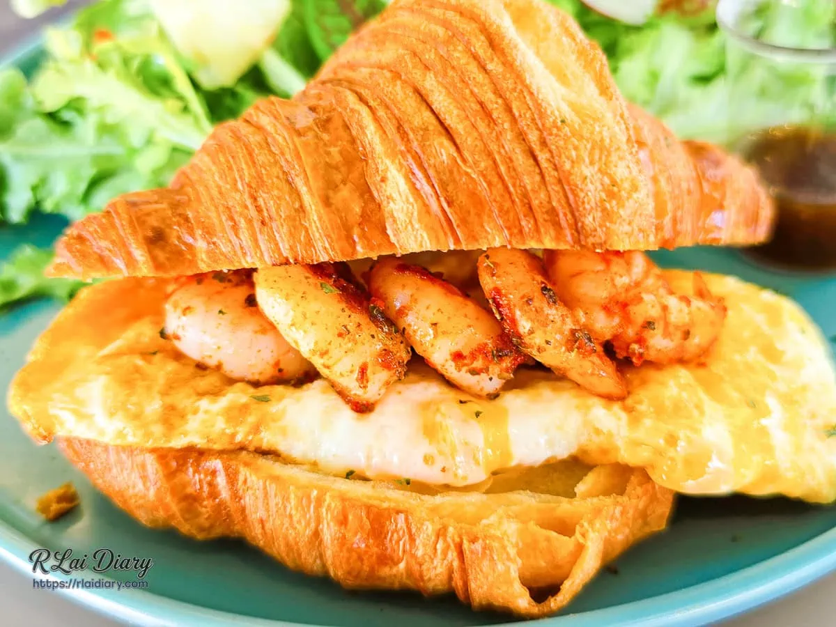 鮮蝦起司可頌斷面特寫，酥脆外皮包裹濃郁起司與海鮮