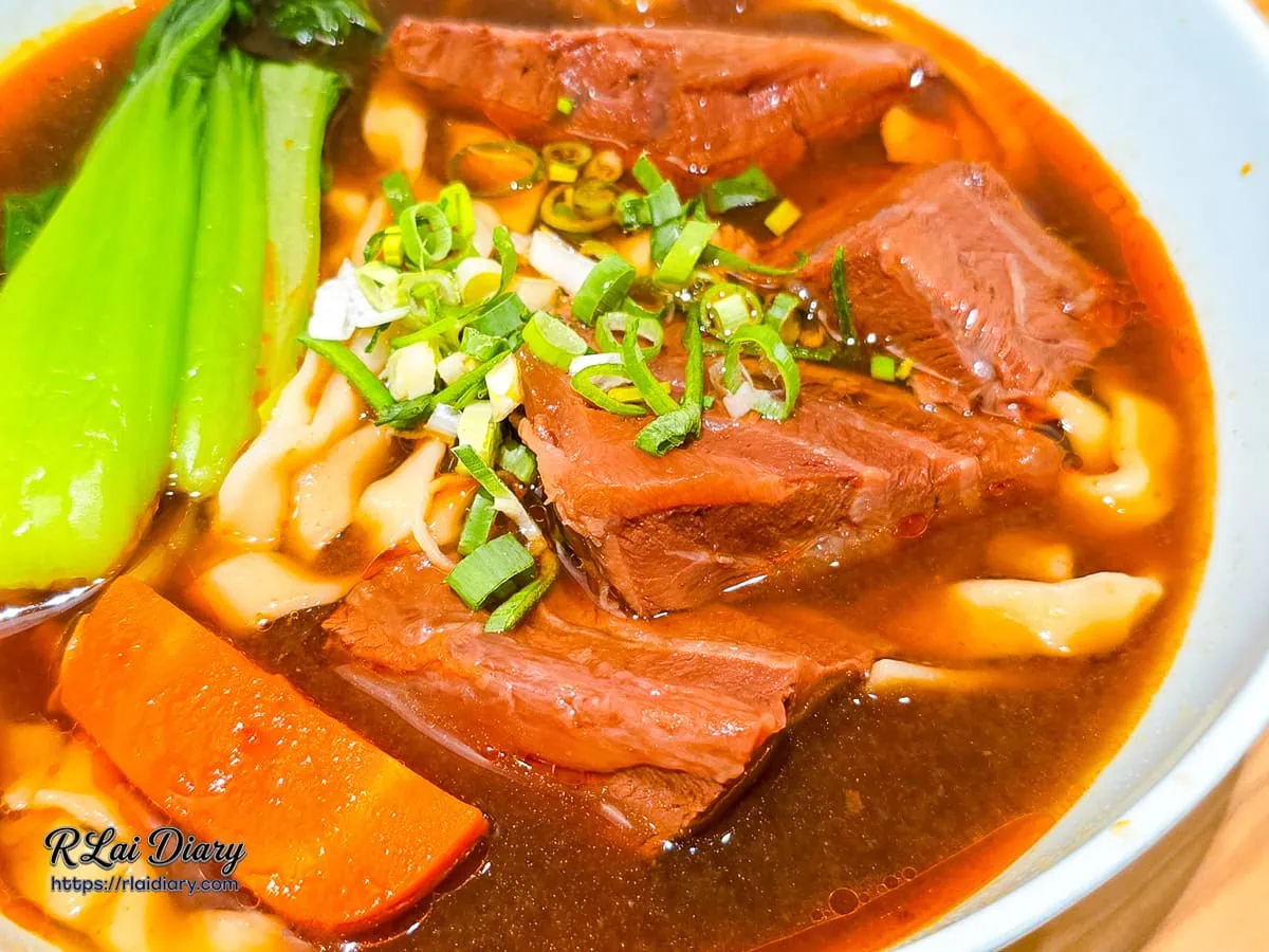 精燉紅燒牛肉麵近拍，展示鮮嫩牛肉塊與蔥花點綴