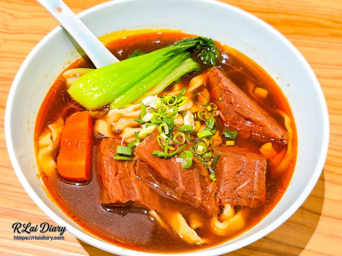 精燉紅燒牛肉麵整碗俯拍，深琥珀色湯頭搭配大塊牛肉與青江菜