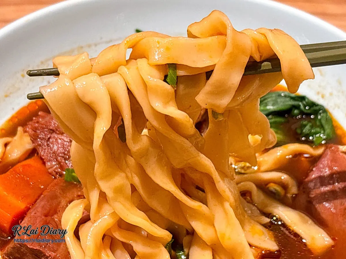 筷子夾起Q彈帶勁的寬麵條，吸附著紅燒牛肉湯汁