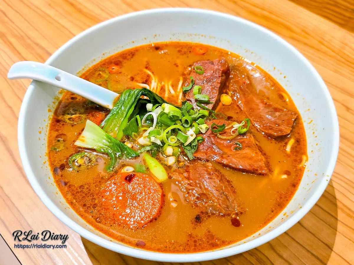 川香麻奶牛肉麵整碗俯拍，橙紅色濃郁湯頭與豐富配料