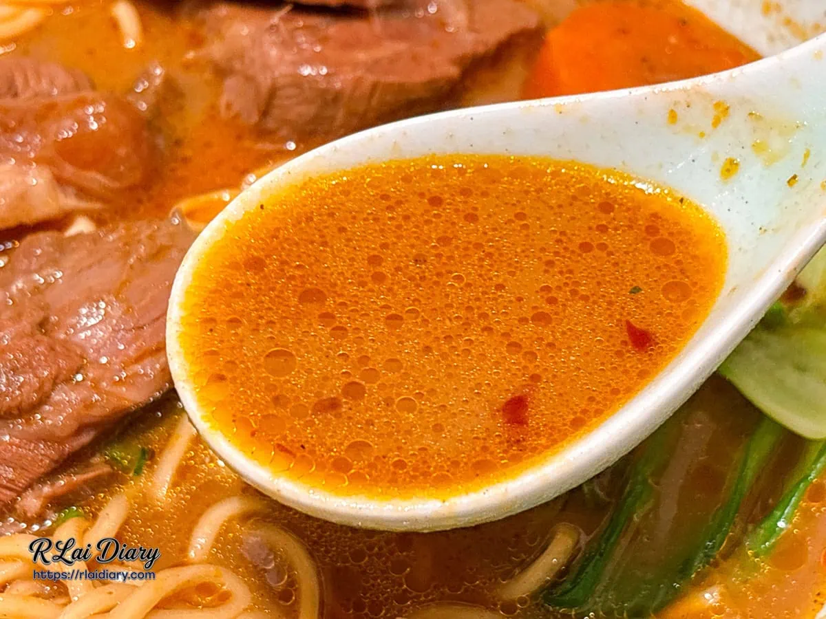 湯匙舀起川香麻奶湯頭，呈現濃郁的金黃橙色澤與油脂