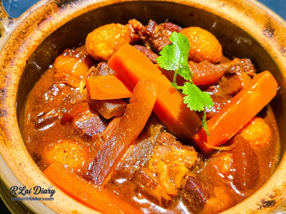 焦香椰汁瓦鍋豬特寫，紅蘿蔔與豬肉浸泡在濃郁醬汁中，撒上香菜點綴