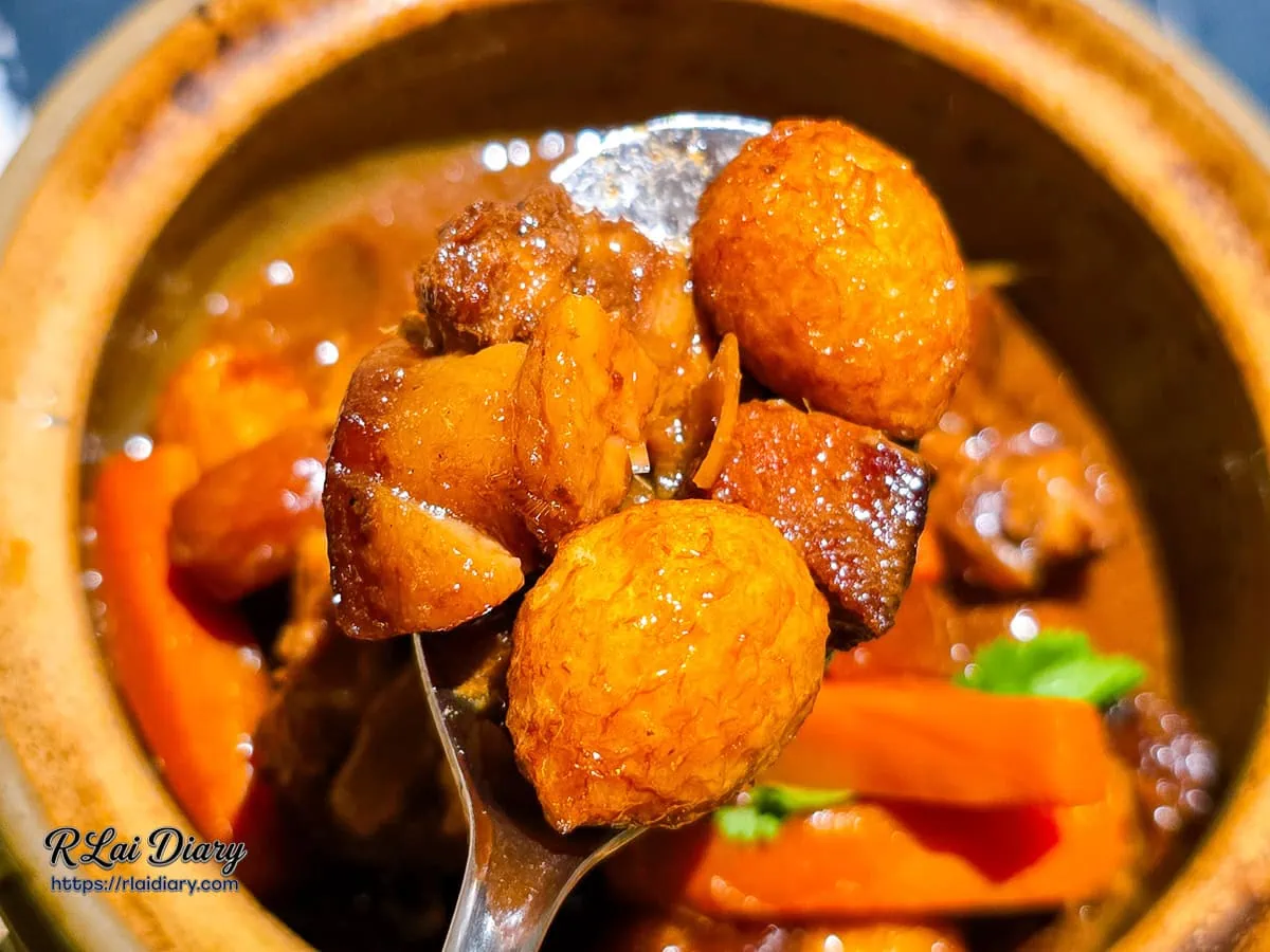 湯匙舀起焦香椰汁瓦鍋豬的肉塊與鵪鶉蛋，展現醬汁的濃稠度與食材光澤