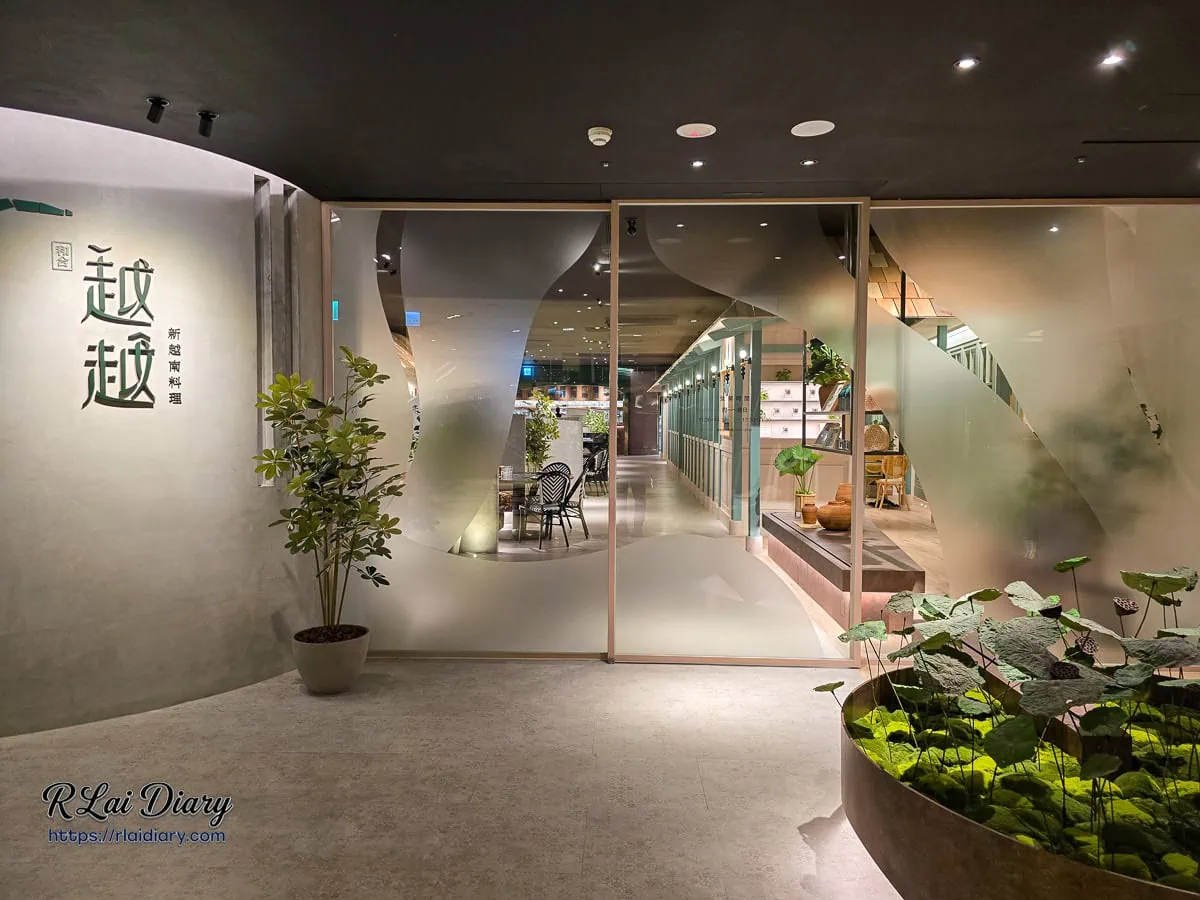 越越品牌 Logo 牆面，搭配綠色植栽與霧面玻璃設計，展現清新質感