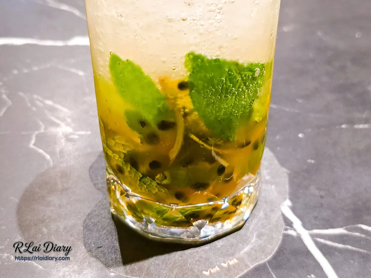 熱帶百香莫西多特寫，可見杯底滿滿的百香果肉與冰塊氣泡，視覺清爽