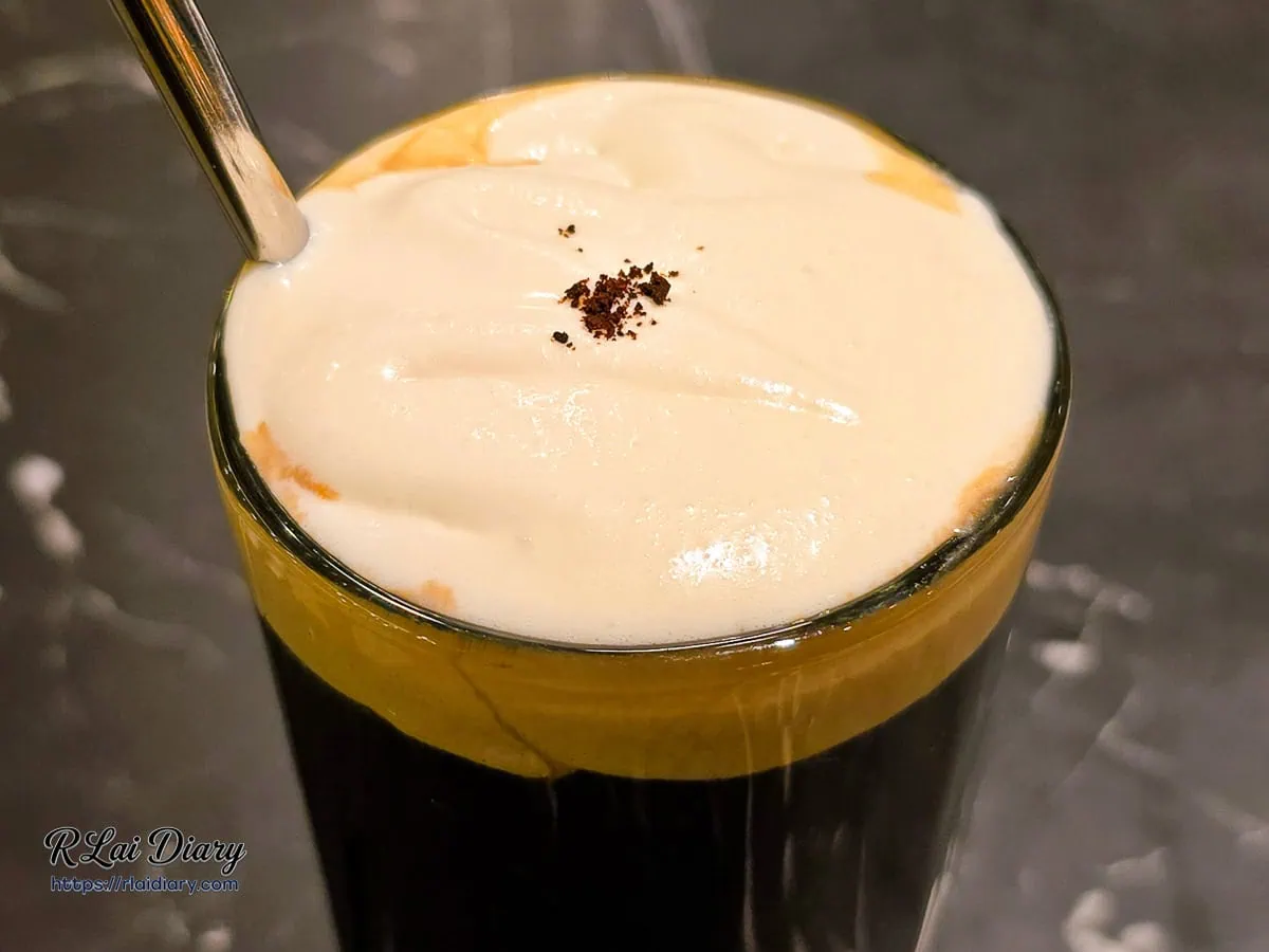 俯拍椰香鹹奶蓋冰咖啡，奶蓋表面撒上些許咖啡粉點綴，層次分明