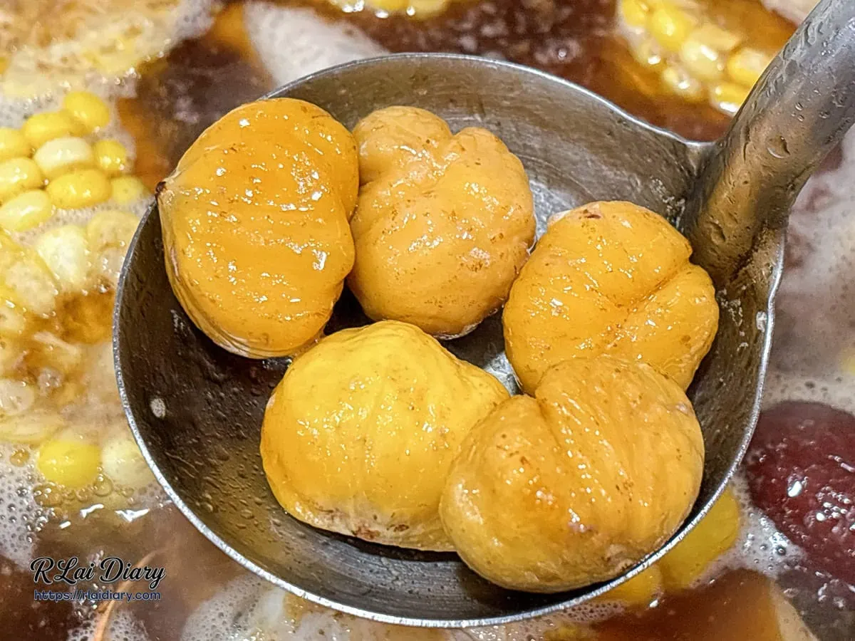 湯匙舀起多顆飽滿的去殼菱角，展現其吸收麻油雞湯汁後的濕潤與鬆軟質地