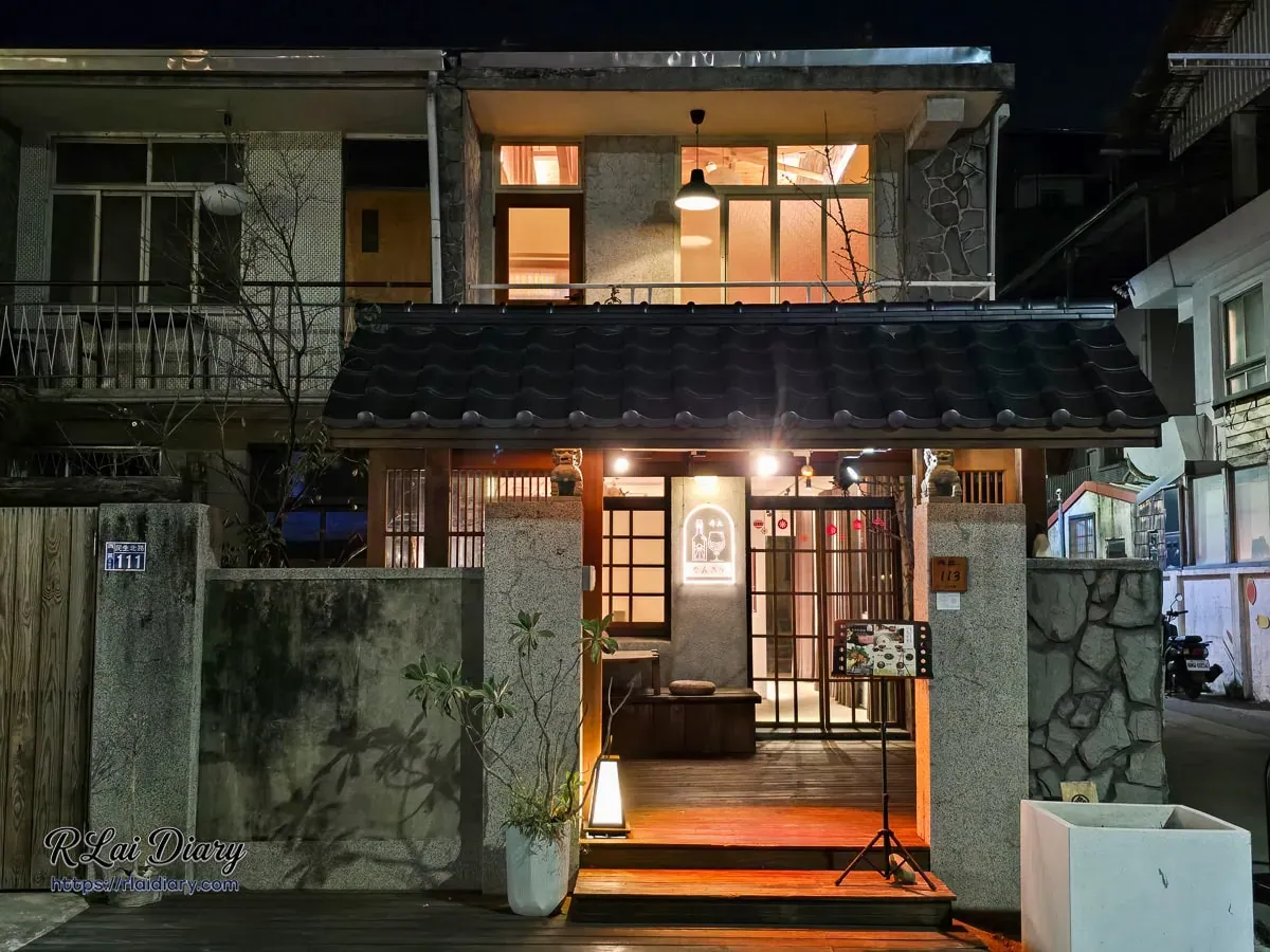 台中丹丘たんきう日式餐廳夜間外觀，溫暖黃光點綴木造建築與特色酒瓶霓虹招牌