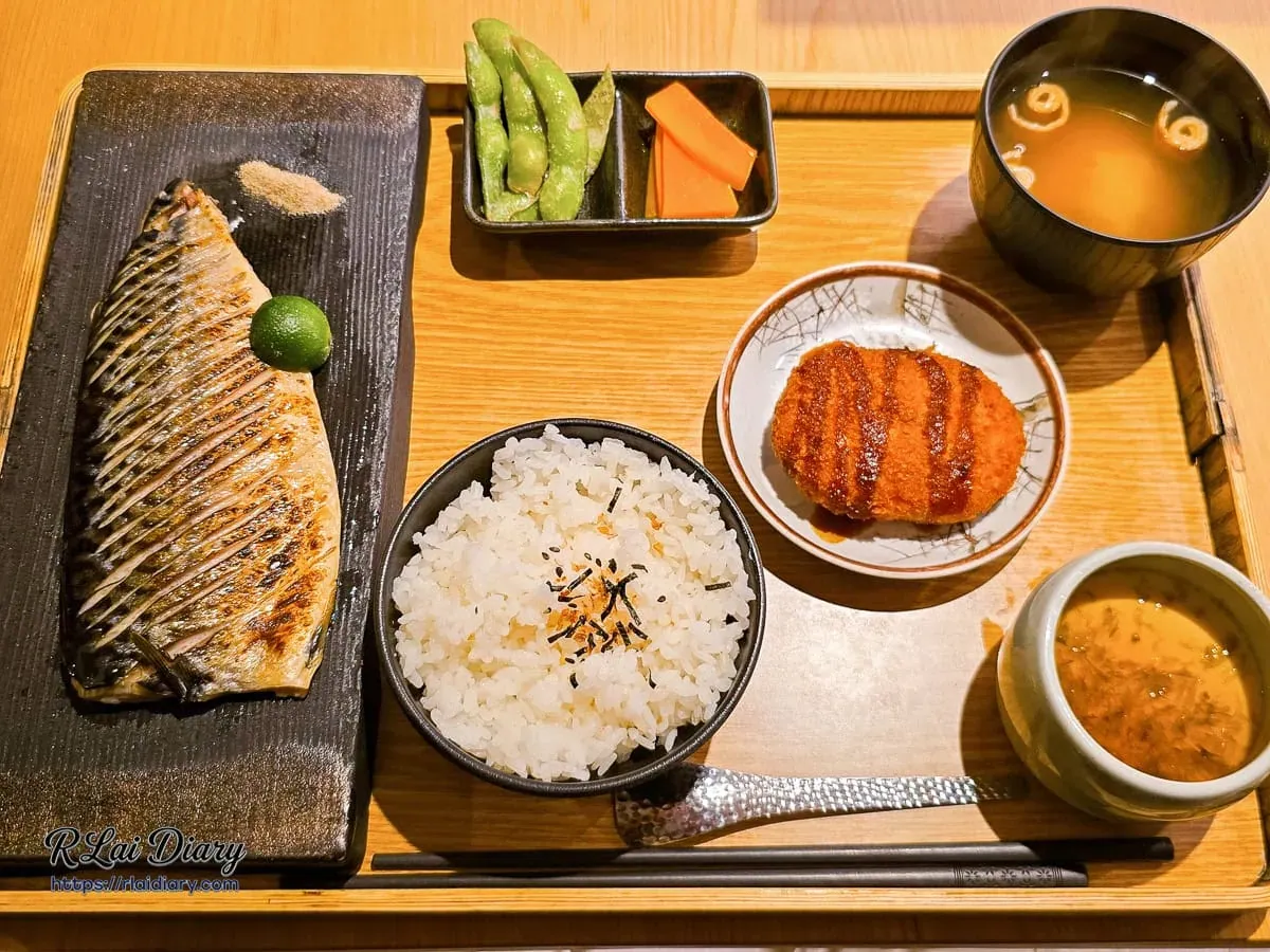 台中丹丘たんきう現烤薄鹽烤鯖魚定食全貌，深色陶盤盛裝金黃鯖魚搭配香米飯與精緻附餐
