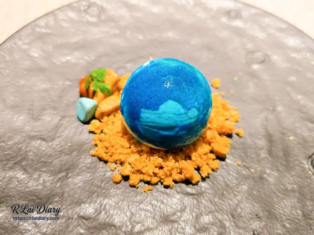 主廚特製地球造型甜點，安座於金黃餅乾碎屑與卵石巧克力上的湛藍星球
