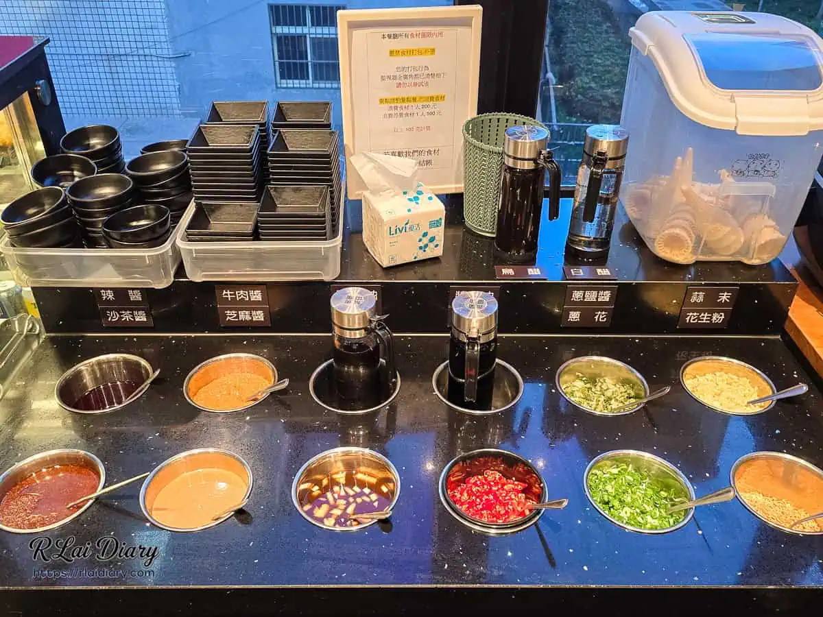 小蒙牛台中大里店醬料吧台，提供芝麻醬、蔥花、蒜末等多樣辛香料，盛裝於金屬圓缽中