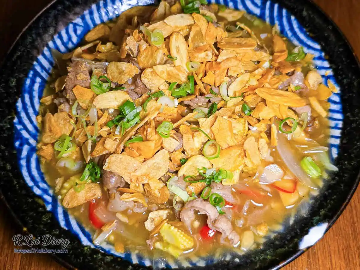 宇貳居酒屋招牌菜奶油蒜香肥牛，鋪滿金黃炸蒜片與蔥花的牛肉料理
