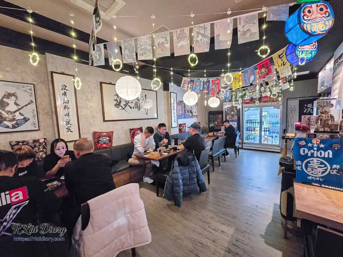 宇貳居酒屋店內用餐環境，懸掛日式燈籠串燈與牆面書法裝飾的溫馨氛圍