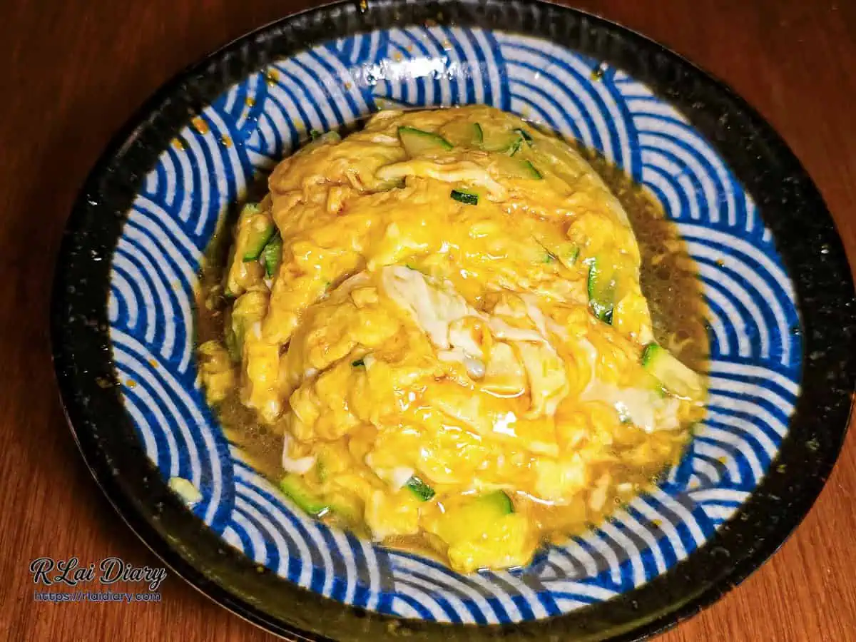 宇貳居酒屋招牌菜櫛瓜嫩蛋，金黃色滑蛋與翠綠櫛瓜俯拍特寫