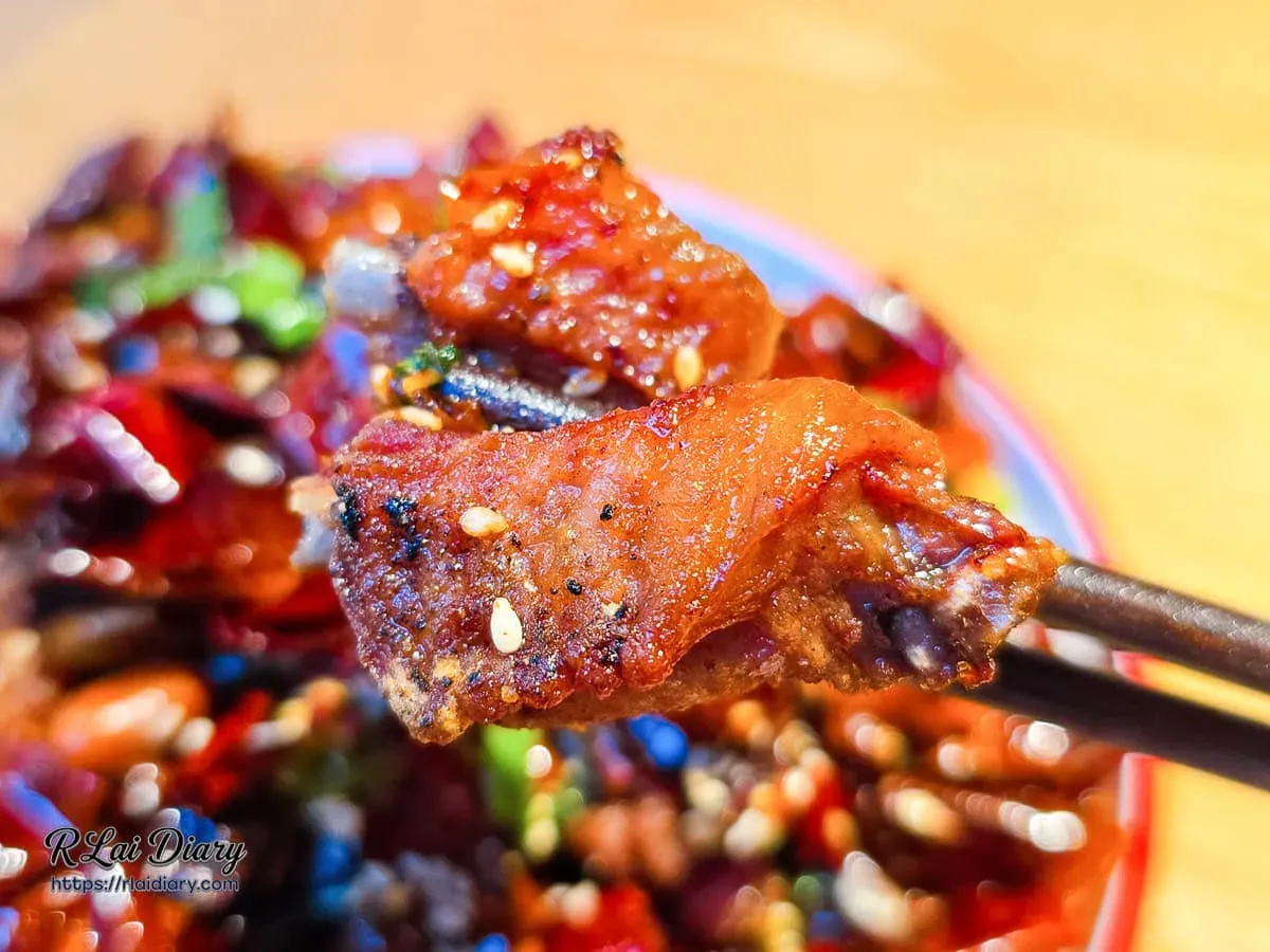 筷子夾起正太酸菜魚辣子雞肉塊呈現焦香色澤與白芝麻顆粒