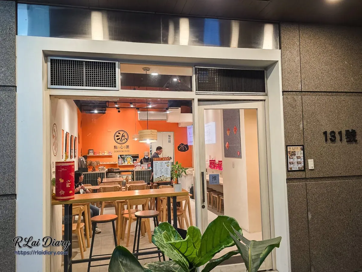 點心源入口處，大片落地窗透出室內活力橘牆與舒適的木質用餐區