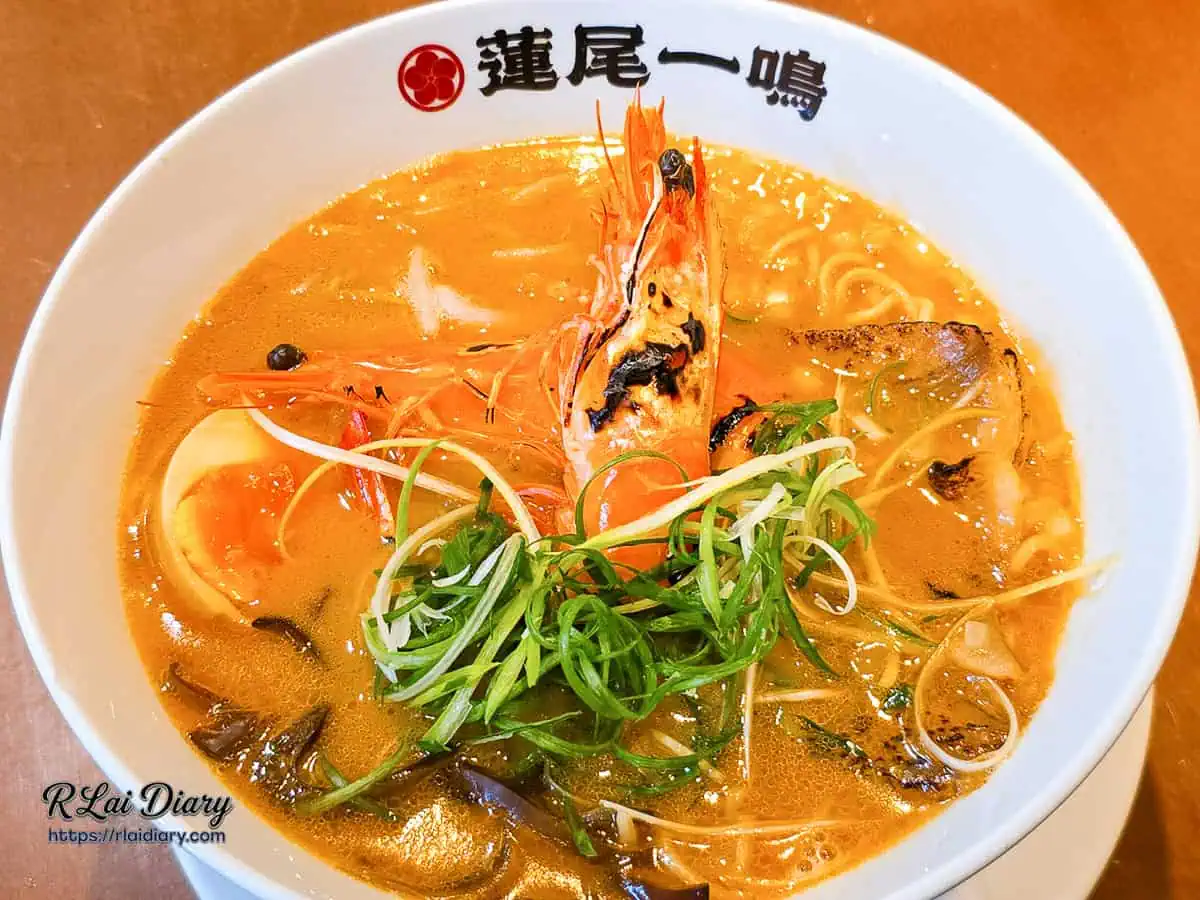 蓮尾一鳴炙叉燒甘海老王樣拉麵全貌，兩尾炙烤大白蝦霸氣盤踞於橘紅色的鮮甜高湯上