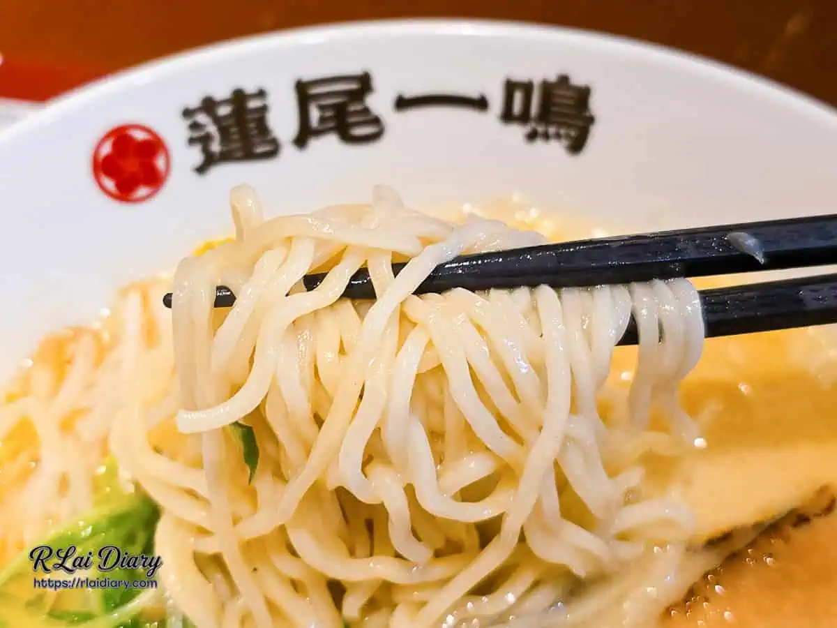 筷子夾起蓮尾一鳴拉麵的細直麵條，麵條完美吸附著濃郁的乳白色豚骨高湯