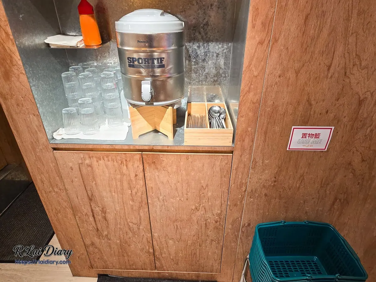 餐廳內提供置物籃與不鏽鋼水桶的整潔自助飲水區細節