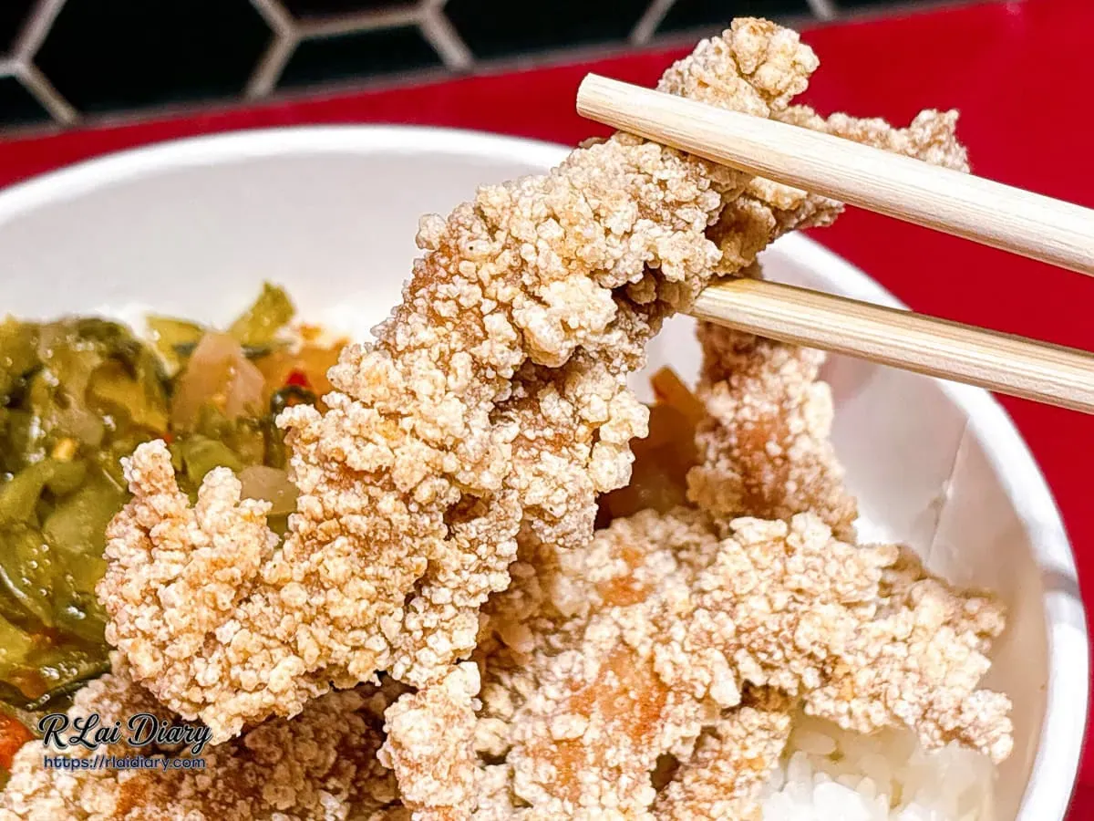 筷子夾起唐山婆古早味炸肉條，呈現外皮空氣感酥脆與內裡鮮嫩纖維的極致特寫
