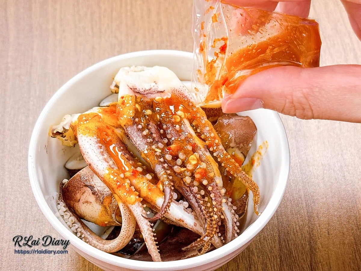 將隨附澄紅透亮的泰式酸辣醬包緩緩澆淋在有飯食光鮮美深海魷魚上的特寫