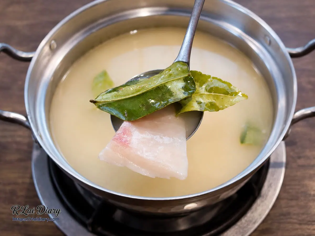 台中西屯火鍋饗鍋物料理神農酸魚鍋，湯杓撈起吸附檸檬葉澄澈酸香與草本精華的鮮嫩魚片特寫